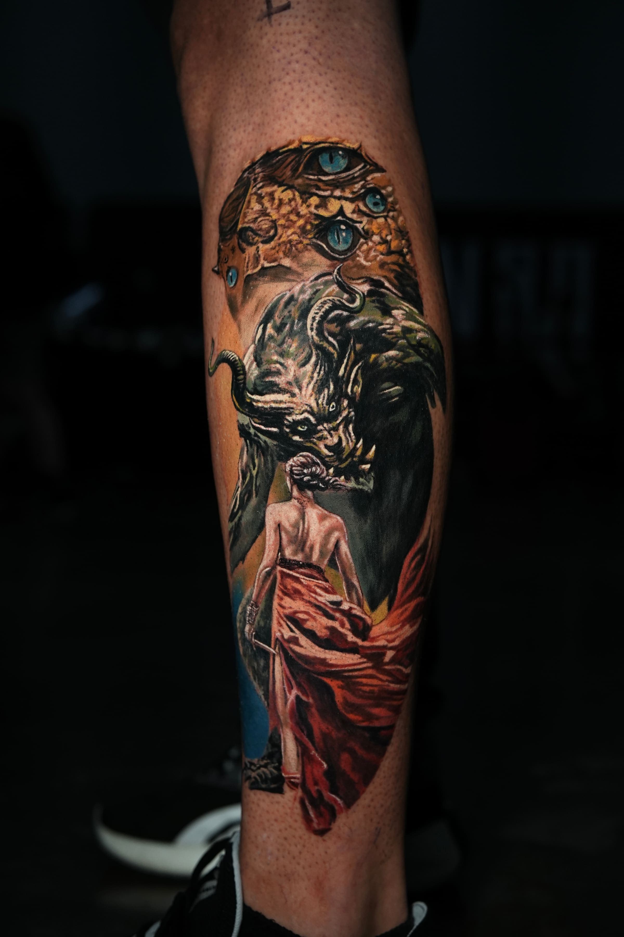 Tatuaje realista a color de una mujer encapuchada frente a un demonio con cuernos, en la pantorrilla, por Rivas Indeed, San Juan, PR